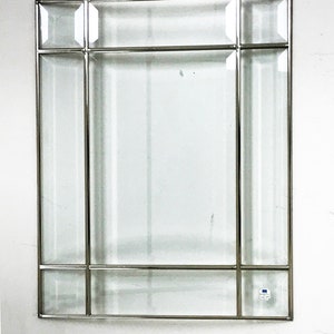May include: Rectangular mirror with a silver metal frame. The mirror features a clear glass surface with a grid-like design. The frame has a geometric pattern with rectangular and square glass panels. The mirror is mounted on a white wall.