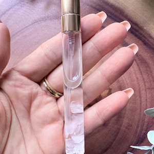 May include: A clear glass bottle with a gold cap and white crystals inside. The bottle is designed for holding essential oils or perfumes.