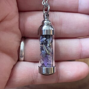 May include: A silver chain necklace with a clear glass vial pendant filled with purple amethyst crystals and dried lavender.