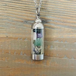 May include: A silver chain necklace with a clear glass vial pendant filled with various small stones, including green, purple, and black.