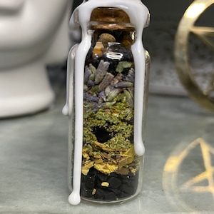 May include: A small glass bottle filled with layers of dried herbs and crystals, sealed with white wax. The bottle is clear and shows the contents inside.