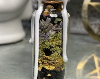Könnte beinhalten: Eine kleine Glasflasche gefüllt mit Schichten getrockneter Kräuter und Kristallen, versiegelt mit weißem Wachs. Die Flasche ist klar und zeigt den Inhalt im Inneren.