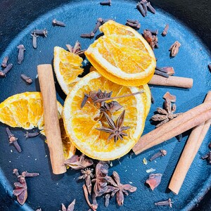 Puede incluir: Una sart&eacute;n de hierro fundido azul llena de rodajas de naranja secas, palitos de canela y estrellas de an&iacute;s. La sart&eacute;n est&aacute; llena de una variedad de especias, incluyendo clavos y an&iacute;s estrellado.