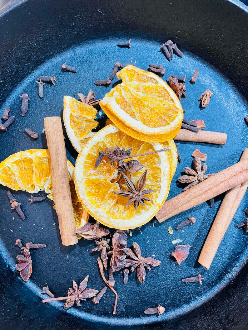 Puede incluir: Una sart&eacute;n de hierro fundido azul llena de rodajas de naranja secas, palitos de canela y estrellas de an&iacute;s. La sart&eacute;n est&aacute; llena de una variedad de especias, incluyendo clavos y an&iacute;s estrellado.