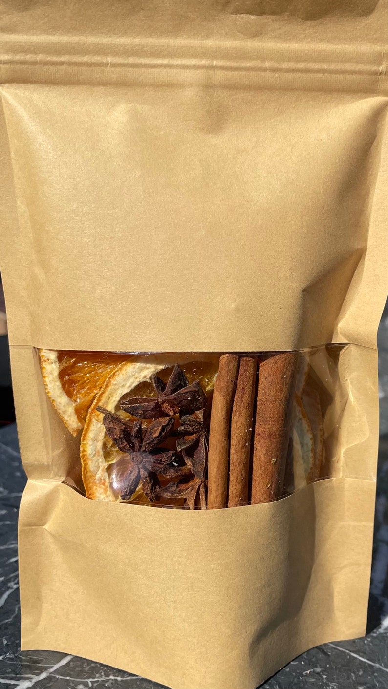 Puede incluir: Una bolsa de papel marr&oacute;n con una ventana transparente que muestra rodajas de naranja secas, an&iacute;s estrellado y palitos de canela en su interior.