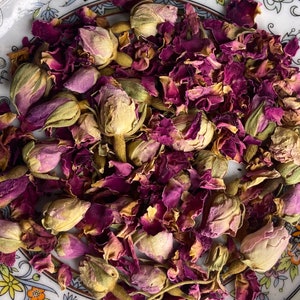 May include: A close-up of dried rose petals and buds in shades of pink, purple, and brown. The petals are scattered and overlapping, creating a textured and colourful background.