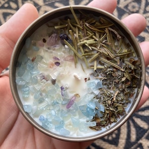 May include: A white candle with blue and purple crystals, dried herbs, and rosemary sprigs embedded in the wax.