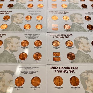 May include: Multiple sets of 1982 Lincoln Cent 7 Variety Sets are displayed. Each set features copper pennies and zinc pennies, with the year 1982 printed on the packaging. The sets include both large and small date varieties.