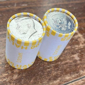以下が含まれることがあります： ケネディハーフダラー硬貨の2つのロール。ロールは白で、黄と白のチェック柄のトリムがあり、側面には「LOOMIS」の文字が印刷されています。各ロールの上部にはコインが見えます。