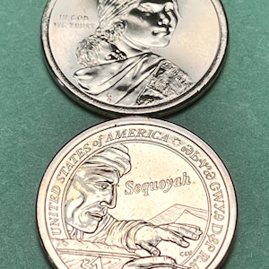 May include: Two United States one-dollar coins. The top coin features Sacagawea with a child on her back, the word LIBERTY, and IN GOD WE TRUST. The bottom coin depicts Sequoyah writing with a quill, the text Sequoyah, $1, and Cherokee syllabary.