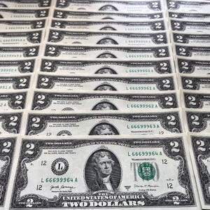 May include: Multiple two-dollar bills arranged in rows. Each bill features a portrait of Thomas Jefferson and the text "Two Dollars." The bills are green and black with the number "2" prominently displayed.