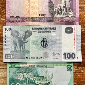 K&ouml;nnte beinhalten: Drei verschiedene Banknoten aus S&uuml;dsudan, Kongo und Malawi. Die s&uuml;dsudanische Banknote ist rosa und lila mit einem Bild eines Elefanten. Die kongolesische Banknote ist gr&uuml;n mit einem Bild eines Elefanten und dem Text "BANQUE CENTRALE DU CONGO". Die malawische Banknote ist gr&uuml;n mit einem Bild eines Elefanten und dem Text "FIFTY KWACHA".