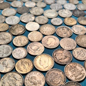 Pode incluir: Uma coleção de moedas antigas, com vários tamanhos e designs, espalhadas sobre uma superfície azul-turquesa. As moedas exibem retratos, inscrições e padrões intrincados, mostrando detalhes numismáticos históricos.