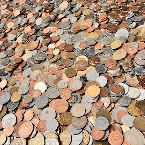 May include: A large collection of assorted metal coins in various sizes, colors, and denominations, scattered across a flat surface. The coins feature diverse metallic finishes including copper, silver, and gold tones, with visible embossed details.