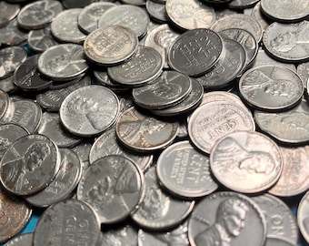 Op de afbeelding: Een close-up van een stapel oude Amerikaanse pennies. De munten zijn zilverkleurig en vertonen tekenen van slijtage en ouderdom. De afbeelding is gevuld met de ronde munten, met de gezichten van Abraham Lincoln en de woorden "ONE CENT" zichtbaar.