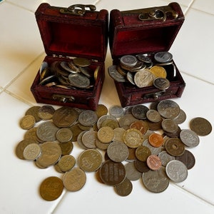以下が含まれることがあります： 金と銀の硬貨がぎっしり詰まった、赤い木製の小さな宝箱が2つ。箱は開いており、硬貨が白い表面にこぼれ落ちている。
