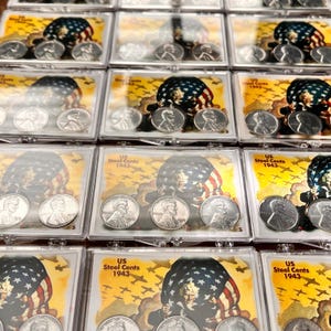 May include: Multiple clear plastic cases, each containing four silver US Steel Cents from 1943. The cases have a patriotic background with an American flag and text that reads "US Steel Cents 1943."
