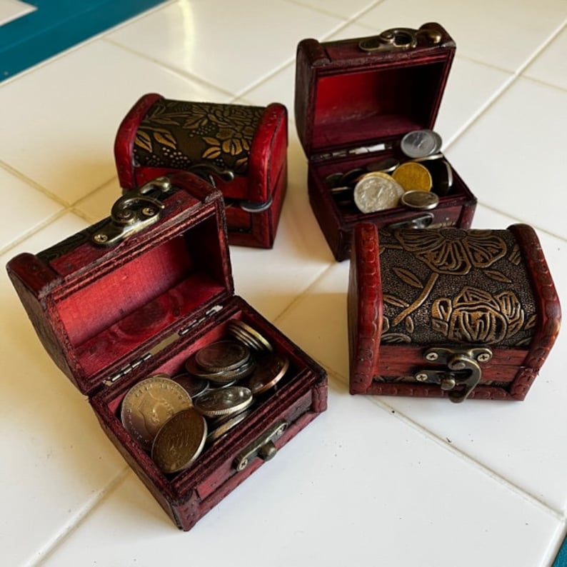 以下が含まれることがあります： 金色の装飾が施された赤い塗りの小さな木製の宝箱が4つあります。3つの宝箱が開いており、コインでいっぱいです。
