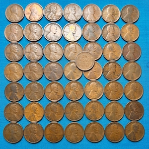 Op de afbeelding: Een verzameling van 64 koperkleurige Amerikaanse één-centmunten, gerangschikt in een rasterpatroon op een blauwe ondergrond. De munten tonen het profiel van Abraham Lincoln en de woorden "ONE CENT" en "UNITED STATES OF AMERICA".