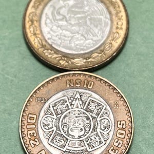 May include: Two Mexican coins. The top coin has a silver center with an eagle design and gold-colored rim. The bottom coin is bronze-colored, with a central design and the words "DIEZ NUEVOS PESOS" and "1993" visible.