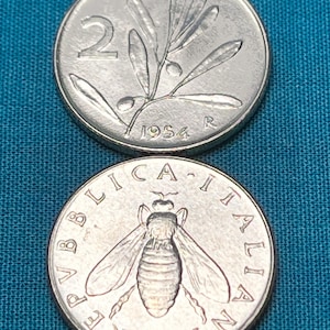 May include: Two Italian coins, one with a bee and the text "REPUBLICA ITALIANA" and the other with an olive branch and the year "1954".
