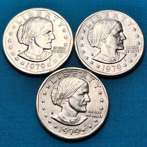 May include: Three silver Susan B. Anthony dollar coins from 1979. Each coin features a portrait of Susan B. Anthony, the inscription "LIBERTY" and "IN GOD WE TRUST", and the year "1979".