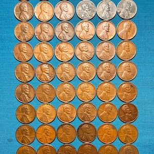 May include: A collection of copper-colored Lincoln pennies arranged in rows on a blue surface. The coins display the profile of Abraham Lincoln. The image includes a white rectangle with the text "Silver State Coin".