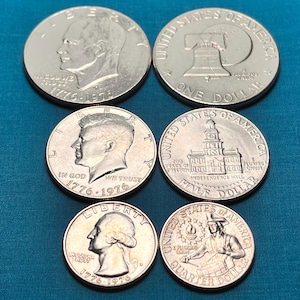 May include: Five silver US coins from 1976, commemorating the bicentennial of the United States. The coins feature different designs, including the Liberty Bell, Independence Hall, and portraits of George Washington, John F. Kennedy, and Susan B. Anthony.