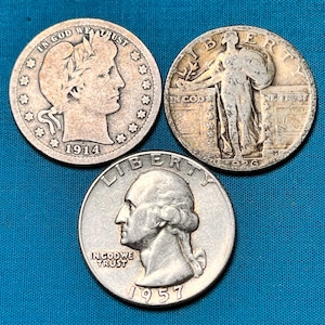 Pode incluir: Três moedas de prata americanas de um quarto de dólar, uma de 1914, outra de 1926 e outra de 1957. As moedas estão dispostas em forma de triângulo sobre uma superfície azul.