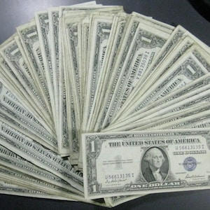 May include: A fan of US one dollar bills, with the text "THE UNITED STATES OF AMERICA" and "ONE DOLLAR" printed on the bills.