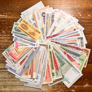 May include: A display of international banknotes arranged in a fan shape on a wooden surface. The notes showcase diverse colours, denominations, and languages, including bills from Vietnam, Japan, and other nations. The banknotes are arranged in a circular pattern.
