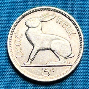 May include: A silver Irish 3 pence coin featuring a hare or rabbit with the inscription "Eire" and "3d" on the coin.