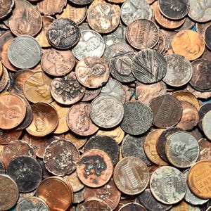 Puede incluir: Primer plano de una pila de centavos estadounidenses. Las monedas presentan varios tonos de cobre, bronce y plata. Algunos centavos están muy desgastados, mientras que otros conservan su brillo original. La imagen muestra los detalles del Lincoln Memorial y el retrato de Abraham Lincoln.