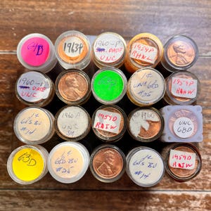 May include: A collection of 16 US penny coins in plastic coin tubes. The coins are from the years 1959, 1960, and 1963. Each tube has a label with the year, mint mark, and condition of the coin.