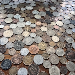 May include: A large collection of various coins from around the world, including silver, copper, and gold coins. The coins are arranged in a random pattern on a wooden surface.