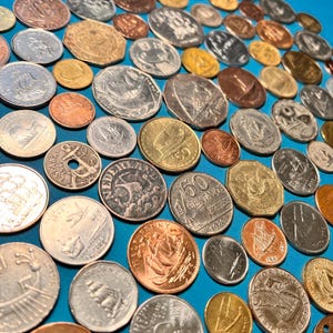 May include: A collection of vintage coins from around the world, featuring a variety of designs and denominations. The coins are arranged on a blue surface, showcasing their unique details and historical significance.