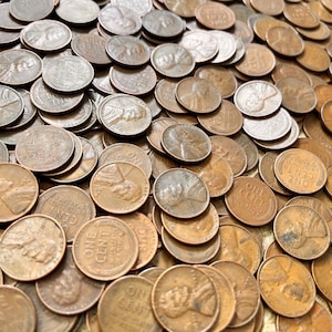 May include: A close-up of a large pile of bronze one-cent coins, also known as pennies. The coins feature the profile of Abraham Lincoln. The words "ONE CENT" and "UNITED STATES OF AMERICA" are visible on some of the coins.