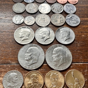 May include: A collection of silver and gold coins, including a variety of U.S. presidents, historical figures, and landmarks. The coins are arranged in rows on a wooden surface.