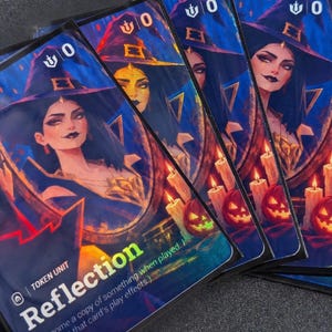 Könnte beinhalten: Ein Satz rechteckiger Spielkarten mit einer digitalen Illustration einer Hexe mit dunklem Haar und spitzem Hut, die sich in einem runden Spiegel spiegelt. Die Karten zeigen den Text Reflection, Token Unit und einen Nullwert.