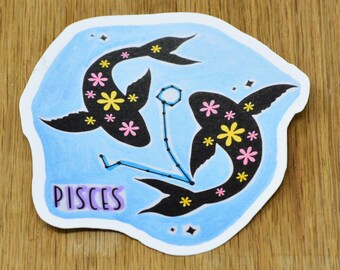 May include: A blue and white sticker with a black silhouette of two fish with floral patterns. The fish are connected by a constellation of stars. The word "Pisces" is written in purple below the fish.