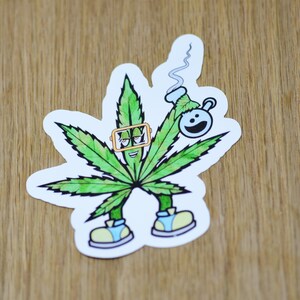 May include: A green marijuana leaf cartoon character wearing goggles and holding a blue bong with a white smoke trail. The character is wearing yellow shoes and has a smiling face.