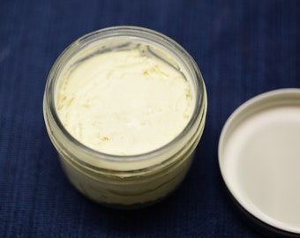 May include: A glass jar filled with a pale yellow cream, with a white lid sitting next to it on a blue surface.