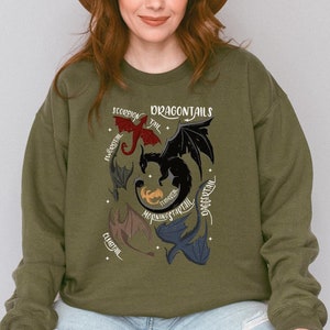 Könnte beinhalten: Ein grünes Sweatshirt mit einem grafischen Druck von fünf Drachen mit unterschiedlichfarbigen Schwänzen. Der Text "Dragontails" ist über den Drachen gedruckt, und die Namen der einzelnen Drachenschwänze sind um die Drachen herum gedruckt.