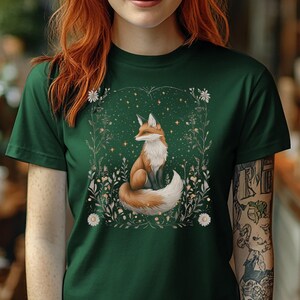 May include: A green t-shirt featuring a graphic of a fox sitting in a field of flowers and stars. The fox is orange and white.