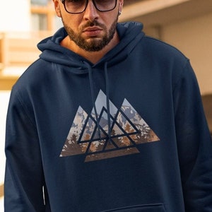 Könnte beinhalten: Ein marineblauer Kapuzenpullover mit einem Grafikdruck eines geometrischen Gebirgszugs in Braun-, Grau- und Blautönen.