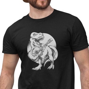 Könnte beinhalten: Ein schwarzes T-Shirt mit einem weißen Aufdruck eines Gitarre spielenden Dinosauriers.