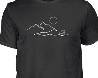 May include: A black t-shirt with a white line drawing of a tractor driving through a landscape with mountains and a sun.