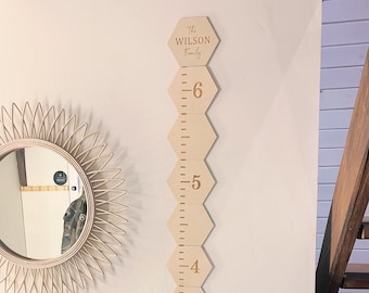 May include: A wooden growth chart with hexagonal pieces, each with a number from 1 to 6. The top piece has the text "The WILSON Family" engraved on it. The chart is mounted on a white wall.