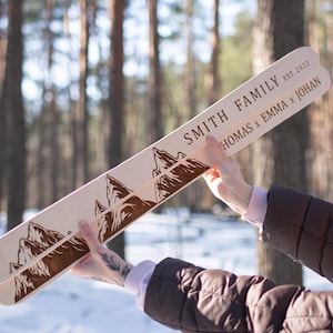 Könnte beinhalten: Ein Paar Holzski mit einem Bergketten-Design und dem Text "SMITH FAMILY EST. 2022 THOMAS x EMMA x JOHAN", der darauf eingraviert ist.
