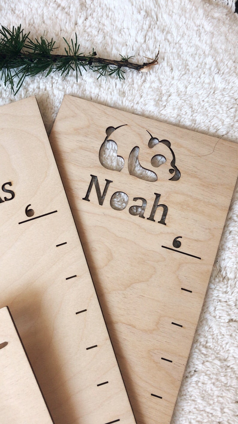Pu&ograve; includere: Un grafico di crescita in legno con un ritaglio a forma di panda e il nome "Noah" inciso su di esso. Il grafico &egrave; contrassegnato per misurare l'altezza in centimetri.